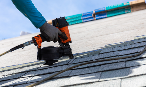 Person using a nail gun on a roof with clear blue sky
